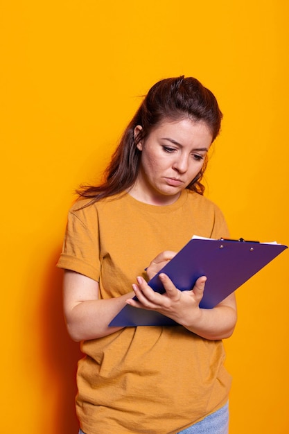 Jongere die aantekeningen maakt over notebookbestanden met pen in studio. Geconcentreerde vrouw die op leerboekpapieren schrijft, documenten ondertekent en papierwerk over project op kladblokklembord.