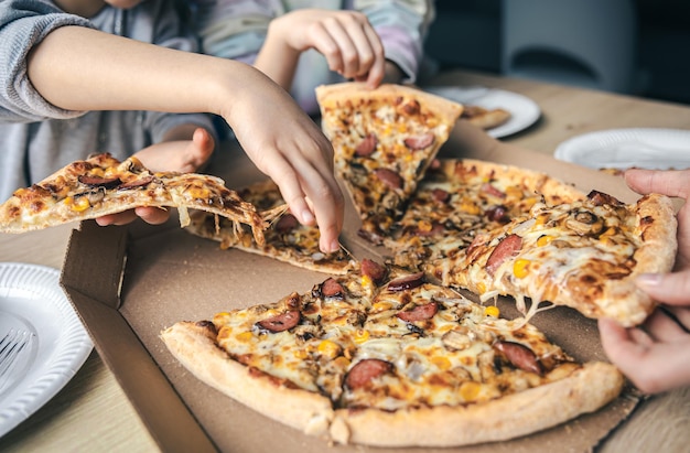 Jongeren nemen sneetjes hete pizza uit kartonnen doos aan tafel