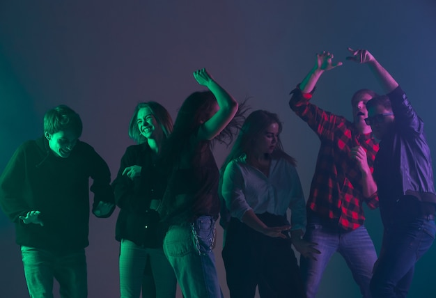 Gratis foto juichend dansfeest, prestatieconcept. menigteschaduw van mensen die dansen met kleurrijke neonlichten stak de handen omhoog op de donkere muur