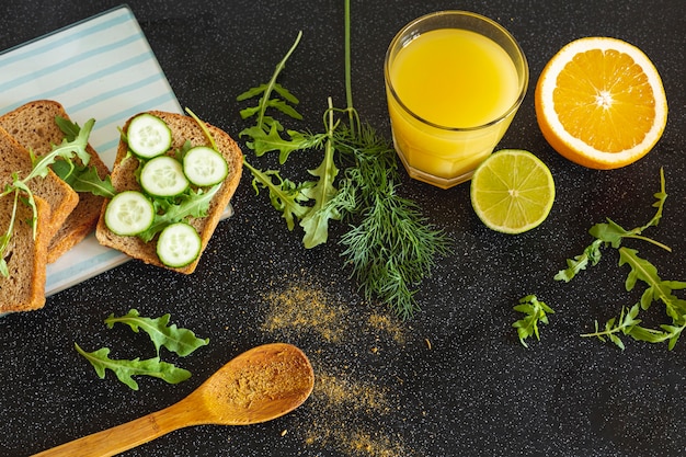 Jus d'orange met een sinaasappelplak en een groentesandwich op een zwarte achtergrond