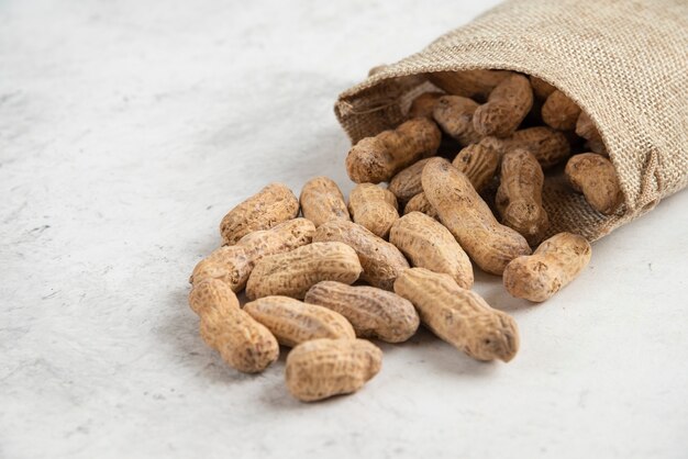 Jute van natuurlijke geroosterde pinda's op marmeren tafel geplaatst.