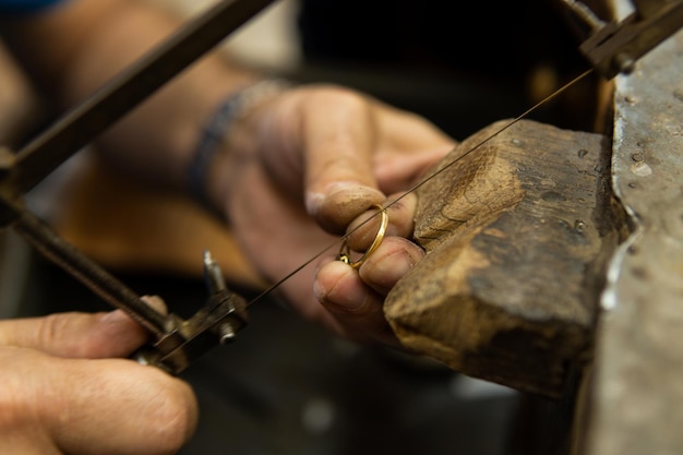 Juwelier aan het werk in zijn atelier om een gouden ring te snijden met een zaag