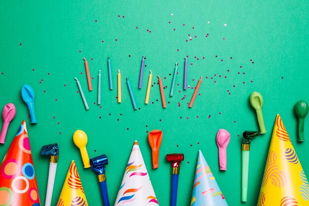 Kaarsen; feesthoed; ballonnen en hoornblazers met confetti op groene achtergrond