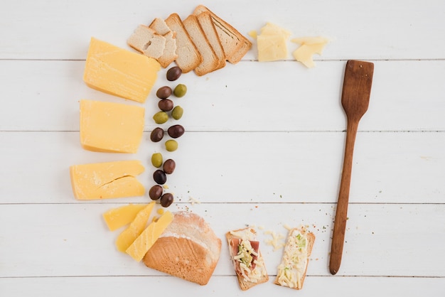 Kaas; olijven en brood voor het ontbijt met houten spatel op plank bureau