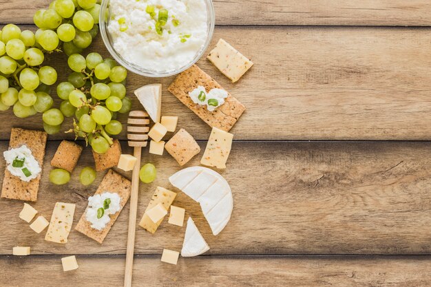 Kaasroomkom, druiven, crackers, kaasblokken en honingsdipper op houten bureau