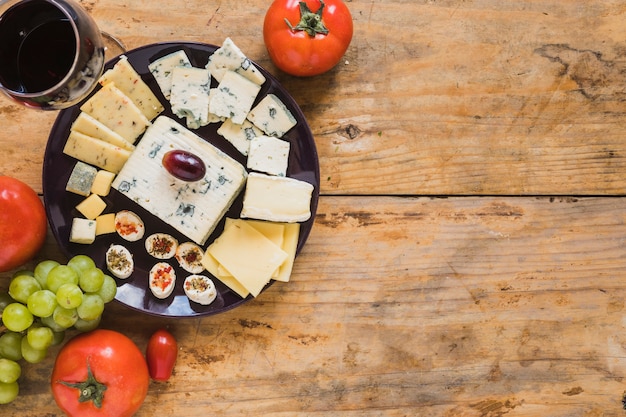 Kaasschotel met tomaten en druiven op houten bureau