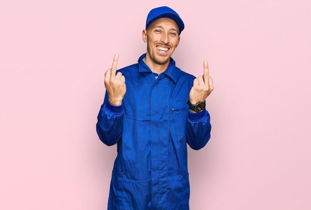 Kale man met baard in jumpsuit-uniform van bouwer met middelvinger die fuck you slechte uitdrukking, provocatie en onbeschofte houding schreeuwend opgewonden doet