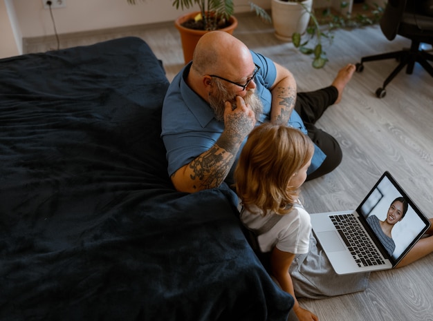 Kale man met schattig klein kind praat met vrouw tijdens videochat via laptop zittend op