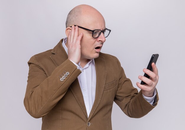 Kale man van middelbare leeftijd in pak met bril kijken naar zijn mobiele telefoon verward