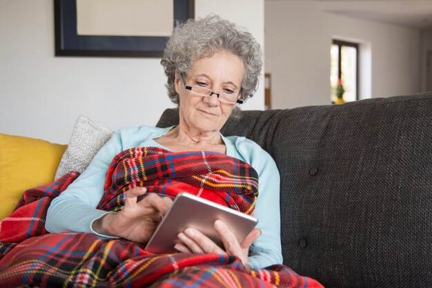 Kalme hogere vrouw die online boek met nieuwsgierigheid leest