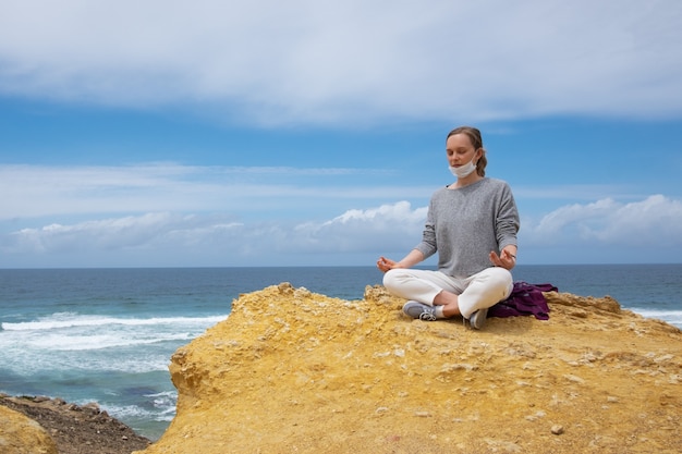 Kalme jonge vrouw in gezichtsmasker die bij oceaan mediteren