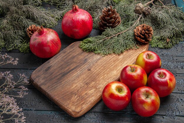 Kant close-up weergave granaatappels en appels twee rijpe granaatappels naast de snijplank vijf appels en takken met kegels op grijze achtergrond