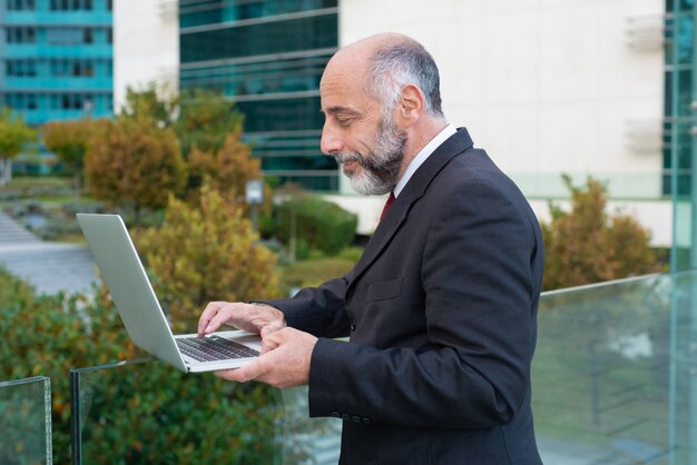 Kant van positieve volwassen bedrijfsleider die met laptop werkt