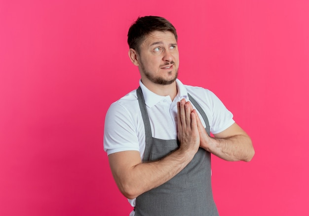 kapper man in schort hand in hand samen zoals bidden of bedelen met hoop expressie staande over roze muur