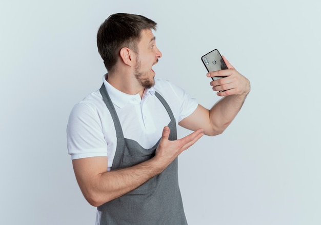 Kapper man in schort houden smartphone kijken opgewonden staande op witte achtergrond