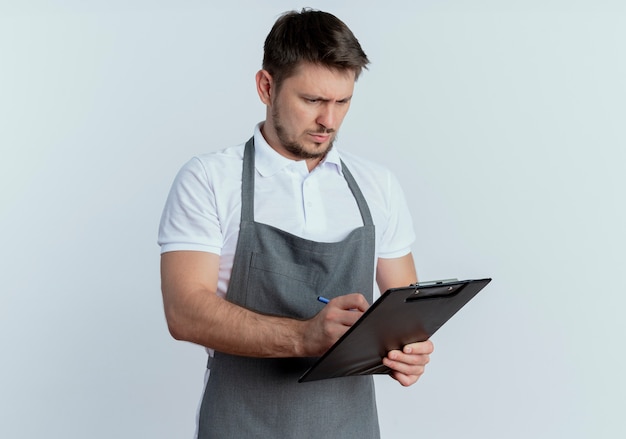 Kapper man in schort klembord houden iets schrijven met ernstig gezicht staande op witte achtergrond