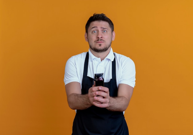 Gratis foto kapper man in schort met baard trimmer bezorgd staande over oranje muur