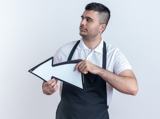 Kapper man in schort met pijl opzij kijkend met een serieus gezicht op een witte achtergrond