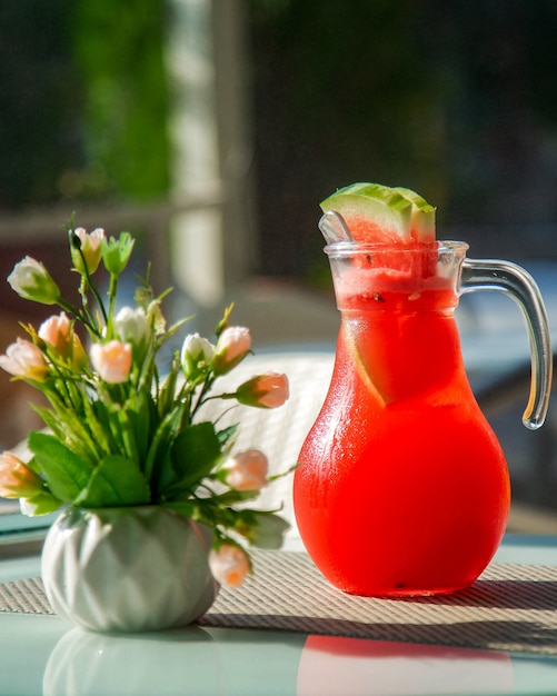 Gratis foto karaf met koud watermeloensap en een vaas met bloemen