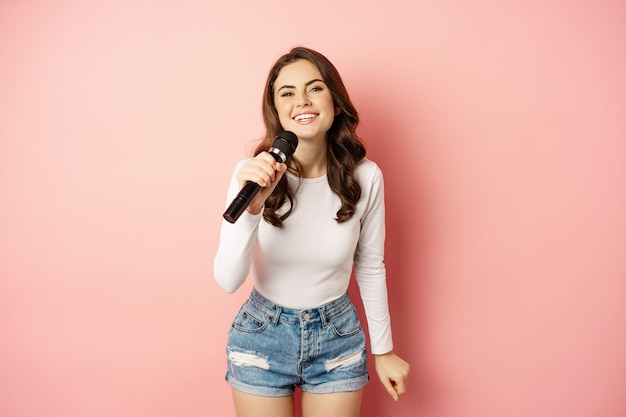 Karaoke. gelukkig lachend meisje zingen in de microfoon, dansen en plezier hebben, staande over roze achtergrond