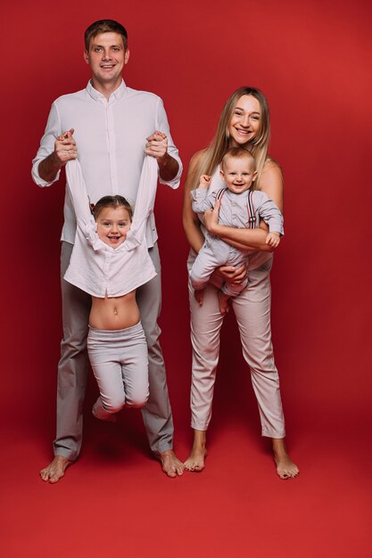 Kaukasisch gezin met twee kinderen poseert samen voor de camera, foto geïsoleerd op rode achtergrond