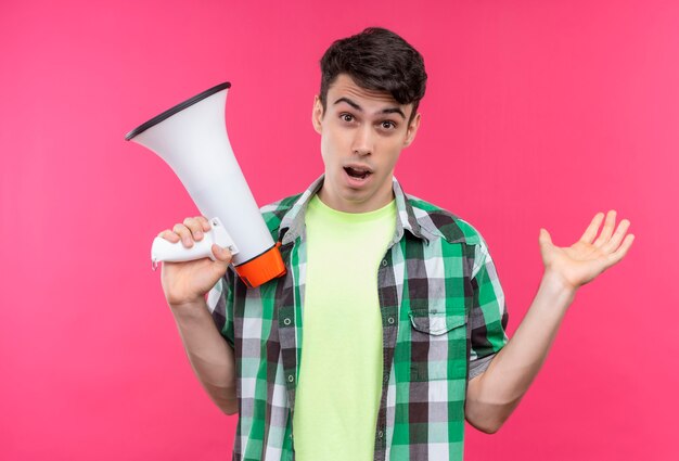 Gratis foto kaukasische jonge man met een groen shirt met luidspreker en opgeheven hand op geïsoleerde roze muur