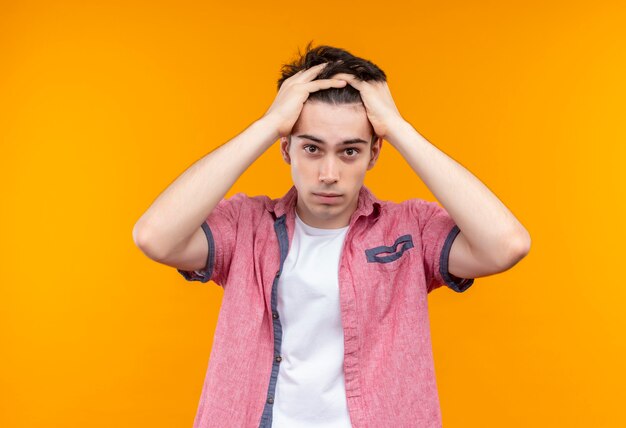 Kaukasische jonge man met roze shirt pakte het hoofd met beide handen op geïsoleerde oranje muur