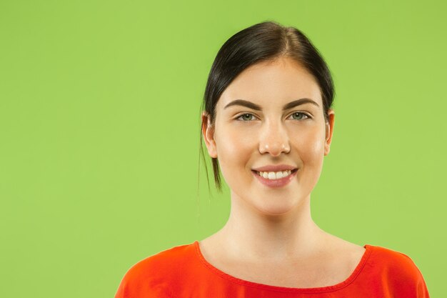 Kaukasische jonge vrouw close-up portret op groene ruimte. Het donkerbruine vrouwelijke model in rood overhemd glimlacht en kijkt gelukkig