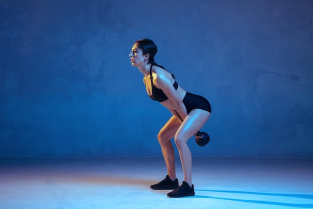 Kaukasische jonge vrouwelijke atleet die op blauwe studioachtergrond in neonlicht oefent Premium Foto