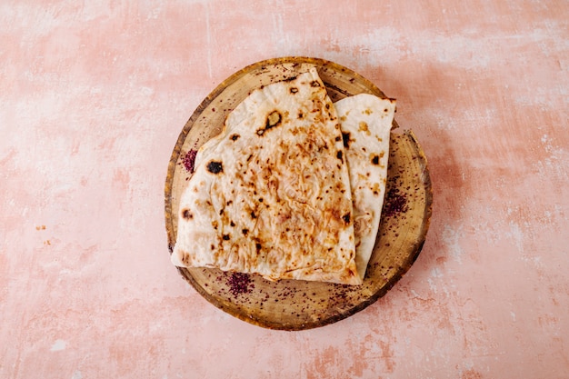 Gratis foto kaukasische lavash kutab met sumakhkruid op een stuk hout op een geweven achtergrond.