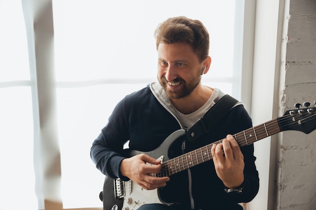 Kaukasische muzikant gitaar spelen tijdens online concert thuis geïsoleerd en in quarantaine, vrolijk improviseren