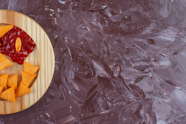 Kegelchips met ketchup in een houten bord, op de marmeren tafel.