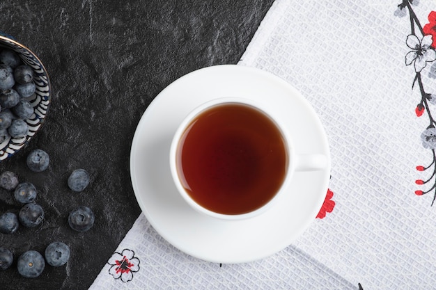 Keramische kom heerlijke verse bosbessen en kopje thee op zwarte ondergrond
