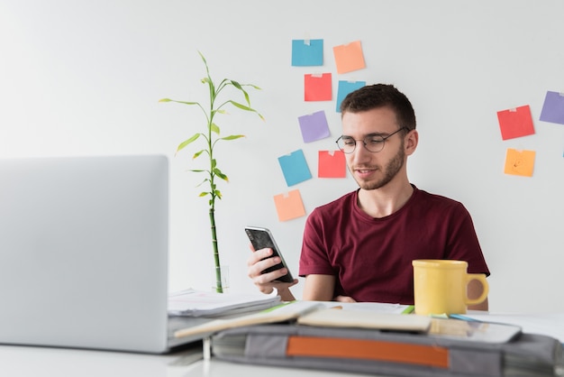 Kerel bij een bureau dat zijn telefoon bekijkt