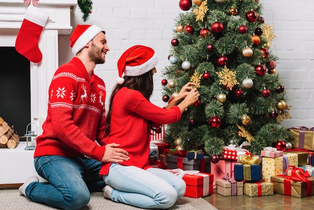 Kerel die dame omhelst die Kerstboom met snuisterijen verfraait