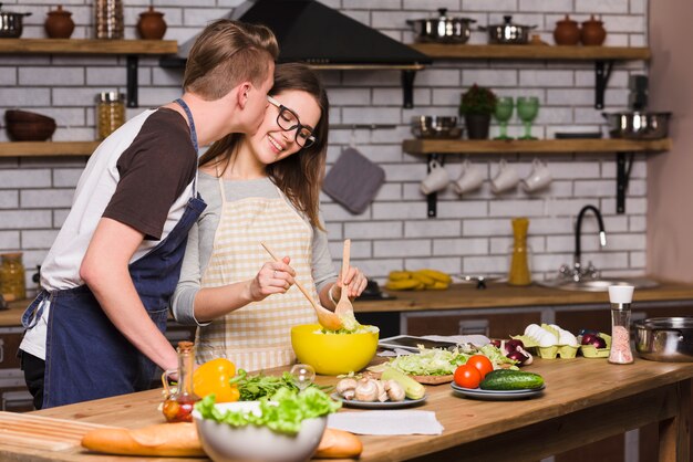 Kerel die jonge vrouw kust die salade in keuken mengt