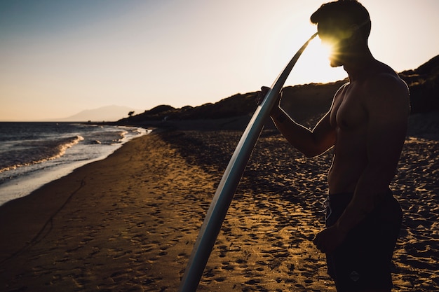 Gratis foto kerel met surfplank bij zonsondergang