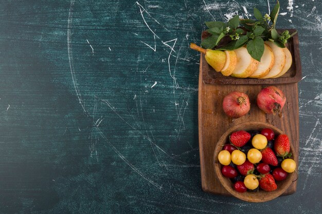 Kersenbordje met granaatappel en peren op een houten schaal aan de rechterkant