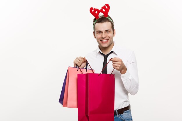 Kerstconcept Knappe zakenman viert prettige kerstdagen en gelukkig nieuwjaar, draagt een rendierhaarband en houdt de rode grote zak van de kerstman vast