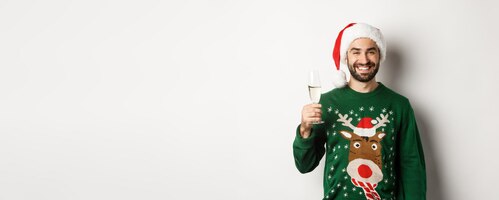Gratis foto kerstfeest en feestdagen concept knappe bebaarde man in kerstmuts en grappige trui ch drinken