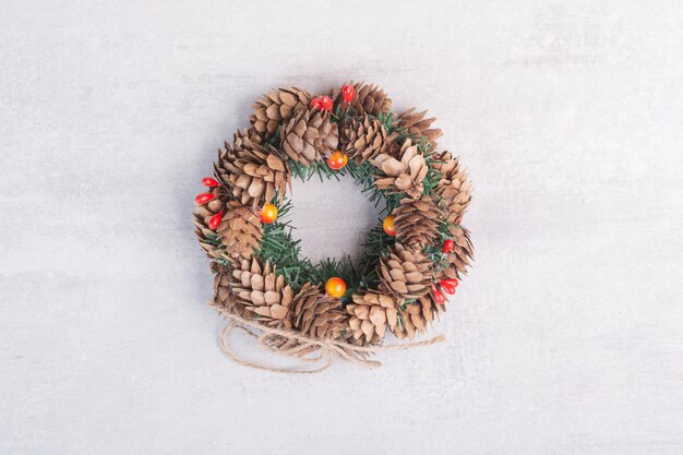 Kerstkrans met rode kralen op witte tafel.