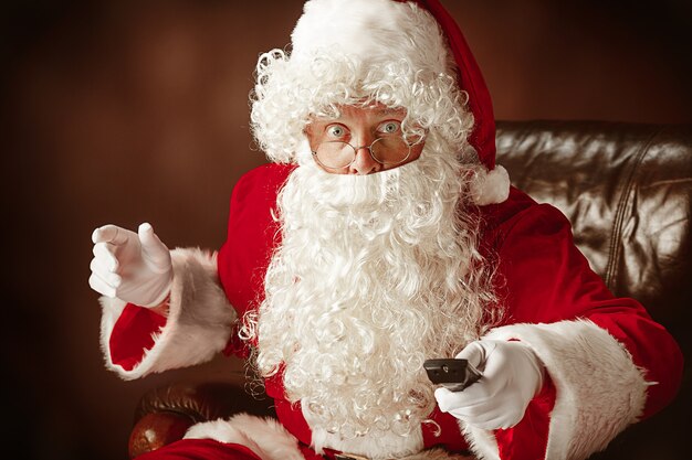 Kerstmankostuum met een luxe witte baard, kerstmuts en een rood kostuum op een rode studioachtergrond