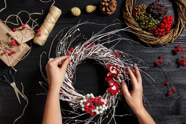 Kerstmis achtergrond. Bovenaanzicht van vrouwelijke handen maken een kerstkrans. Verpakte geschenken en rollen, vuren takken en gereedschappen op houten tafel. Werkplek voor het voorbereiden van handgemaakte decoraties.