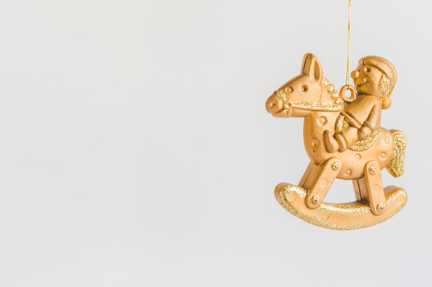 Kerstmisornament met gouden beeldjezitting op hobbelpaard tegen witte achtergrond