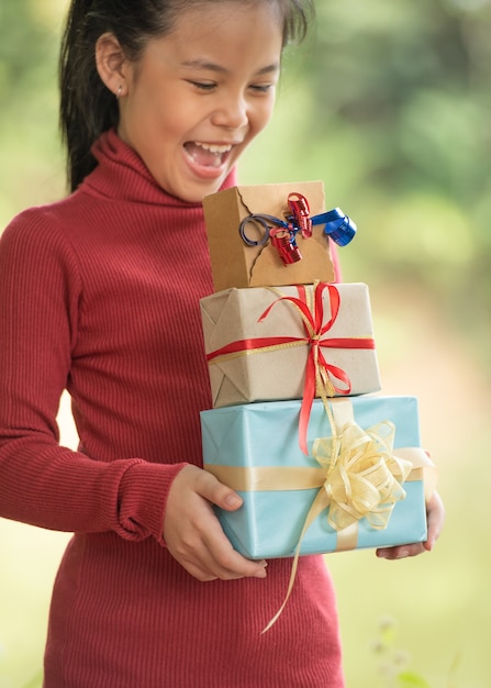 Kerstportret van een gelukkig lachend klein meisje met een geschenkdoos in de buurt van een groene takboom. groene bladeren bokeh onscherp achtergrond van natuur bos.