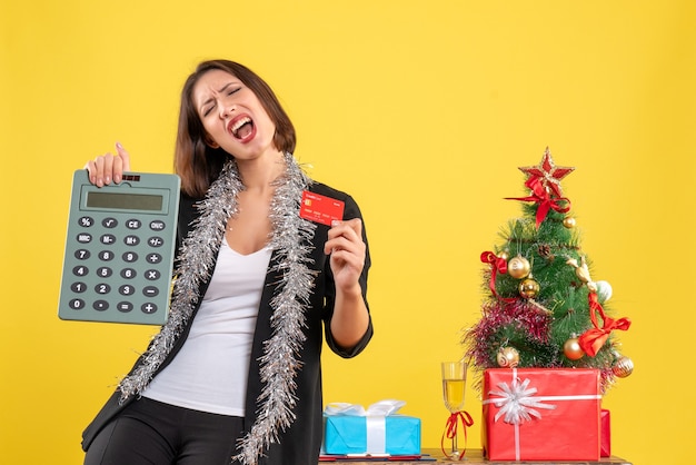 Kerstsfeer met emotionele mooie dame permanent in het kantoor en rekenmachine bankkaart in het kantoor op geel te houden