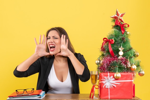 Kerstsfeer met jonge gespannen zakelijke dame die iemand belt en op kantoor zit op geel