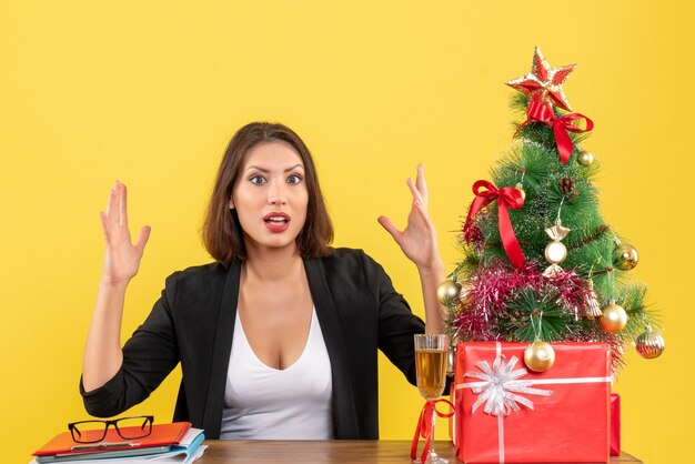 Kerstsfeer met jonge ontevreden serieuze emotionele bedrijfsdame die op geel verschijnt