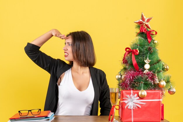 Kerstsfeer met jonge ontevreden serieuze emotionele zakendame die zorgvuldig iets op geel bekijkt