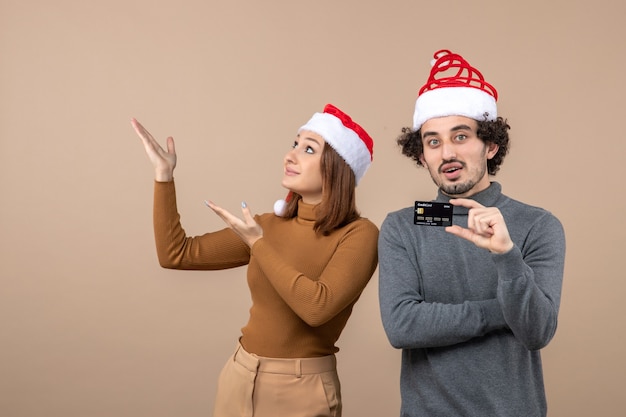 Kerstsfeer met opgewonden gelukkig koel paar dat rode hoeden van de Kerstman draagt die bankkaart toont